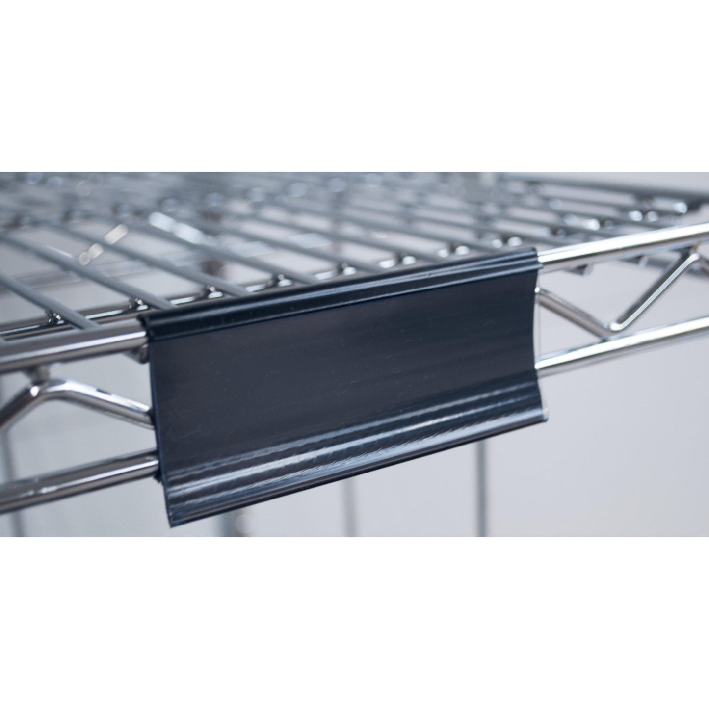 Close-up van een Novocal etiketframe met papieren labels (ca. 100 x 44 mm, 1 stuk), bevestigd aan een metalen draadrek, met de zwarte kunststof etikethouder aan de voorkant; de achtergrond is wazig.