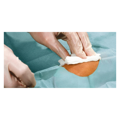 Un gros plan de mains gantées nettoyant une petite zone de peau avec un chiffon blanc, entourée de champs opératoires Hartmann Foliodrape® Protect, autoadhésifs, stériles, emballés individuellement, de la société Paul Hartmann AG.