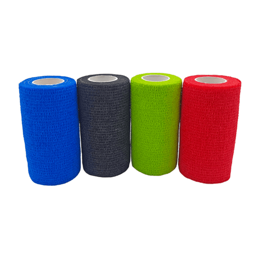 Vier rollen Holthaus VliVet® zelfklevend verband voor diergeneeskundig gebruik van Holthaus Medical GmbH & Co. KG liggen naast elkaar op een rij. Van links naar rechts zijn de kleuren blauw, zwart, groen en rood. De verbanden hebben een gestructureerd oppervlak en een cilindrische vorm met een witte binnenkern, ideaal voor de hoefverzorging in de diergeneeskunde.