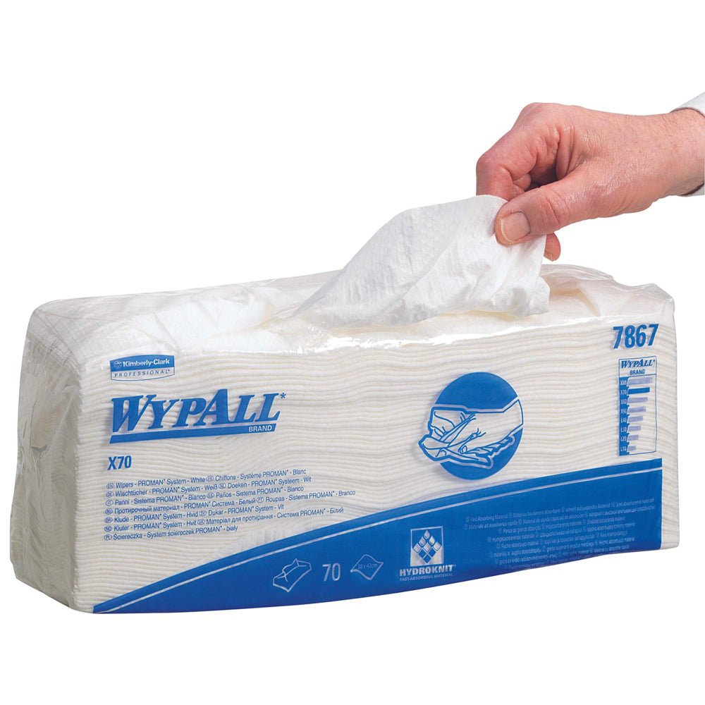 Une main tire une lingette WypAll® X70 d'un emballage rectangulaire portant l'inscription "WypAll® X70" (70 lingettes, 6 sacs/carton) de Kimberly-Clark GmbH. L'emballage principalement blanc est orné de texte et de graphiques bleus pour le nettoyage industriel.