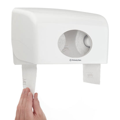 Une main tire les rouleaux de papier toilette Kleenex® de la société Kimberly-Clark GmbH (blanc, 8 paquets x 12 petits rouleaux, 250 feuilles chacun) d'un distributeur à double paroi avec une fenêtre ovale - idéal pour une utilisation avec ce carton (8 paquets).