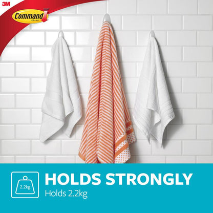 Trois serviettes sont suspendues à des crochets pour serviettes de bain Command™ de 3M Deutschland GmbH - une serviette rayée orange et blanche entre deux blanches - sur un mur carrelé blanc. Texte : "HÄLT STARK Supporte 2,2 kg." Logos Command et 3M visibles.