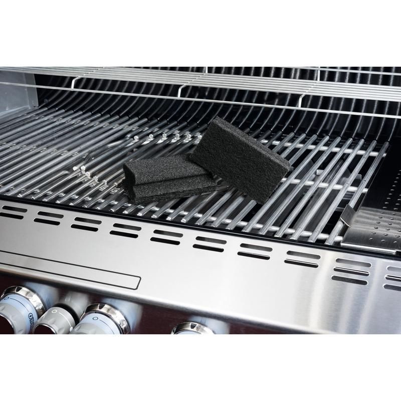 Een Scotch-Brite® Grill Greepspons van 3M Deutschland GmbH ligt op een roestvrijstalen grill en benadrukt de eenvoudige grillreiniging. Op het rooster zijn de zwarte sponzen, grillknoppen en het geopende deksel zichtbaar.