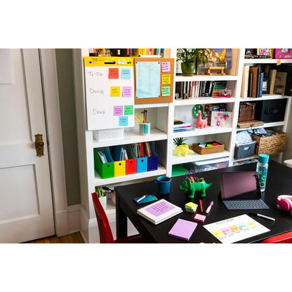 Een thuisbureau met een zwart bureau, een rode stoel en planken met boeken en opbergruimte. Op het bureau liggen een iPad, notitieboeken, pennen, een waterfles, een groene dinosaurusfiguur en 3M Post-it® Super Sticky Notes (47,6x47,6mm, 90 vel/Blok, 100% PEFC).