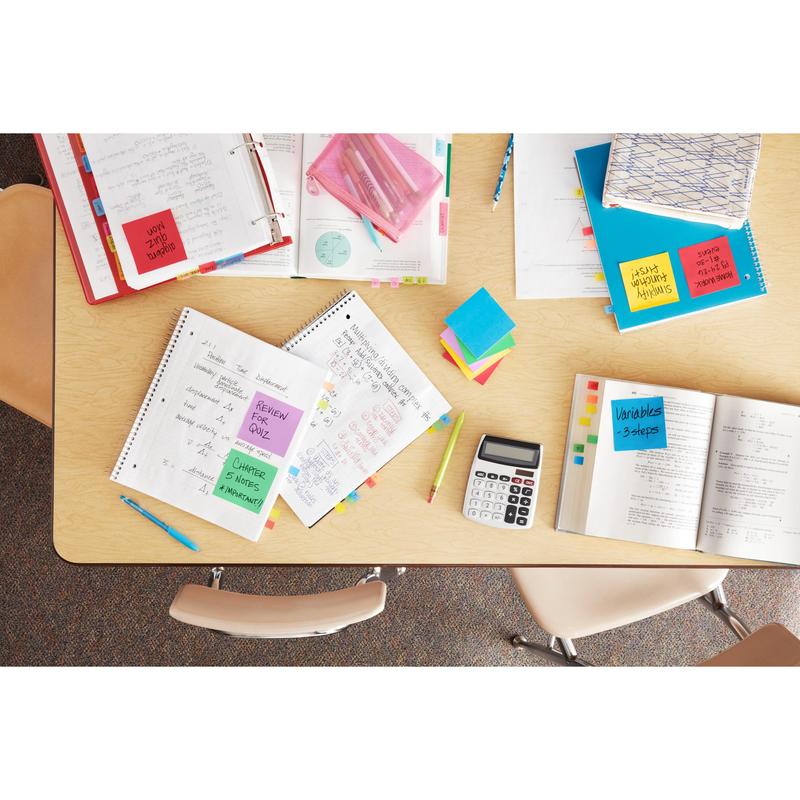 Une table avec des cahiers ouverts, des stylos, des classeurs et une calculatrice est vue de dessus. Les papiers sont organisés avec des Post-it® Super Sticky Z-Notes de 3M (différentes couleurs néon, 76x127mm) pour une consultation rapide; trois chaises vides entourent la table.