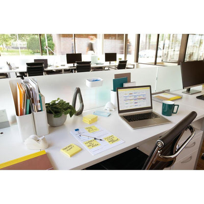 Un bureau moderne avec un ordinateur portable, des notes Post-it® 3M (jaune, 76x76 mm, 100 feuilles/bloc), une tasse, des documents, des plantes et des accessoires sur un bureau blanc. À l'arrière-plan, d'autres bureaux et de grandes fenêtres sont visibles.
