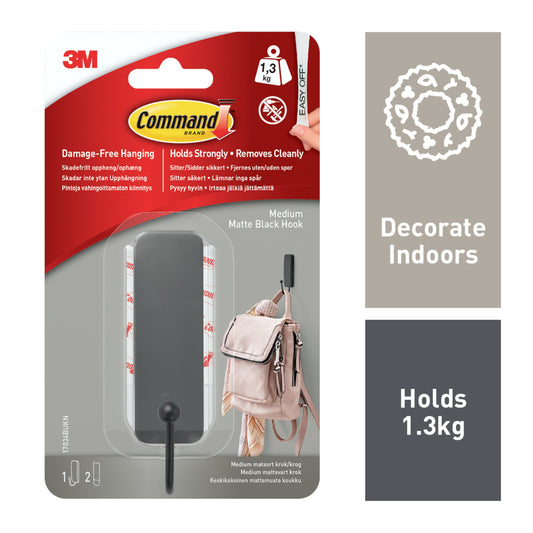 Der mittelgroße Command™ mattschwarze Haken (17034B) von 3M Deutschland GmbH wird in Originalverpackung gezeigt: Er trägt bis zu 1,3 kg, ist leicht ablösbar und für den Innenbereich geeignet. Ein Bild zeigt den Haken mit einer Tasche.