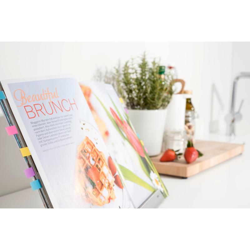 Un livre de cuisine ouvert avec une recette de brunch marquée par une mini bande adhésive Post-it® Index de 3M Deutschland GmbH. En arrière-plan, des fraises, un pot d'herbes et des ustensiles de cuisine sont disposés sur une planche en bois sur un plan de travail blanc.