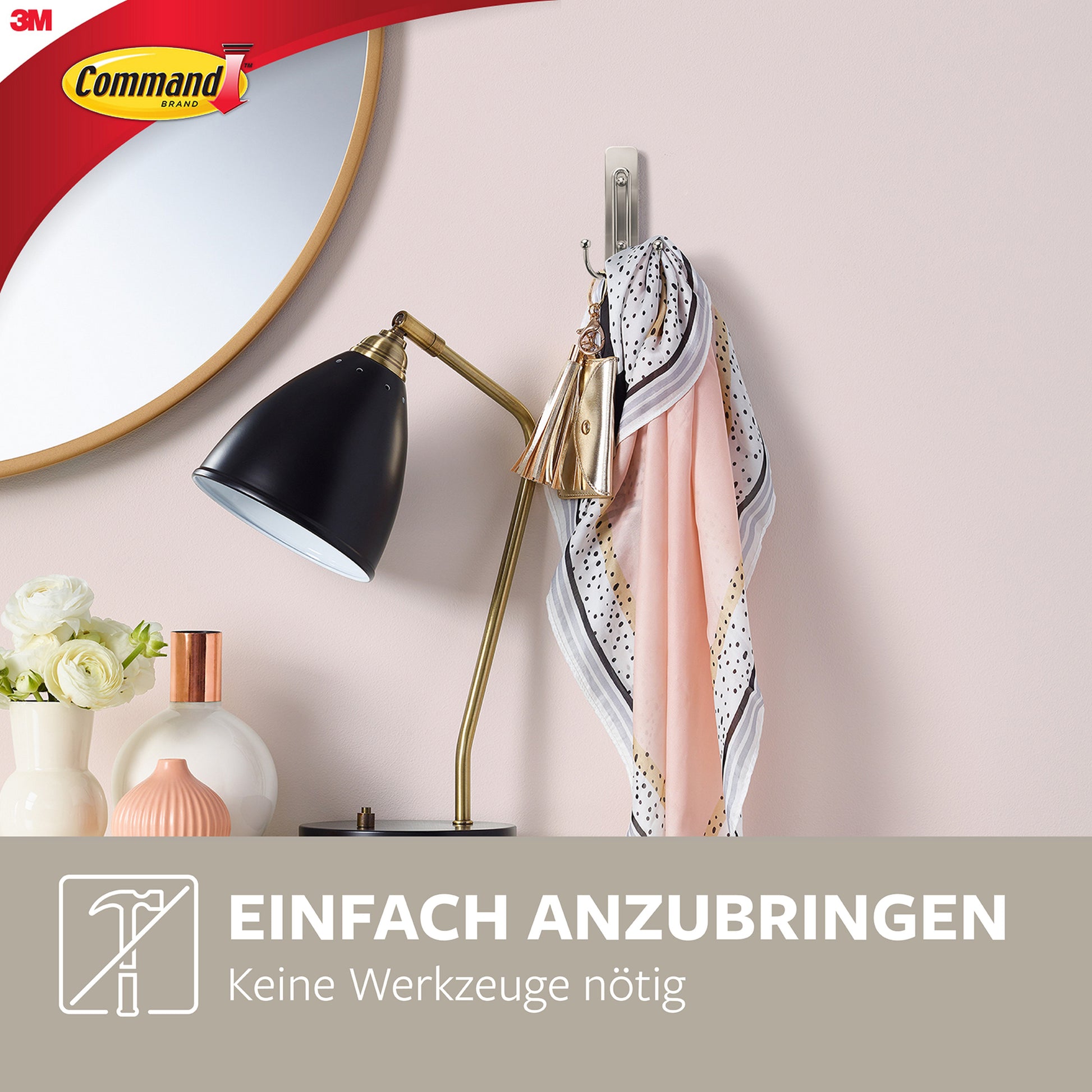 Ein überdimensionaler Schal und ein Schlüsselbund hängen am 3M Deutschland GmbH Großer Command™ Doppelhaken in gebürstetem Nickel (17036) an einer hellrosa Wand über einem Schreibtisch mit einer schwarzen Lampe, Blumen und Vasen. Deutscher Text: "Einfach anzubringen. Keine Werkzeuge nötig.