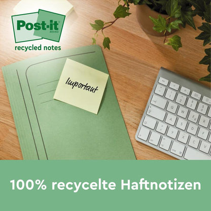Une chemise verte avec un Post-it® Super Sticky 100% recyclé jaune (47,6 x 47,6 mm, 70 feuilles/bloc, PEFC) de 3M Deutschland GmbH portant l'inscription "important" est posée sur une table en bois à côté d'un clavier et d'une plante. Le texte est en allemand.