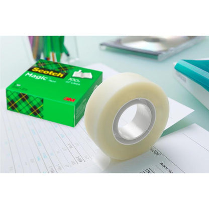 Een rol Scotch® Magic™ Onzichtbare Tape van 3M Deutschland GmbH in zijn groene verpakking ligt op documenten op een bureau, terwijl pennen, een notitieboek en andere kantoorbenodigdheden op de achtergrond wazig te zien zijn.