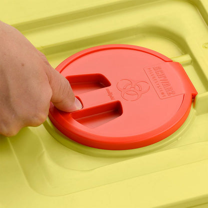 Een hand drukt op het rode deksel van een gele 12-liter afvalcontainer van Helmut Schwarz GmbH melijekt (20 stuks per karton), waarop het biohazard-symbool en de tekst SHARPMAX" zijn gegraveerd.