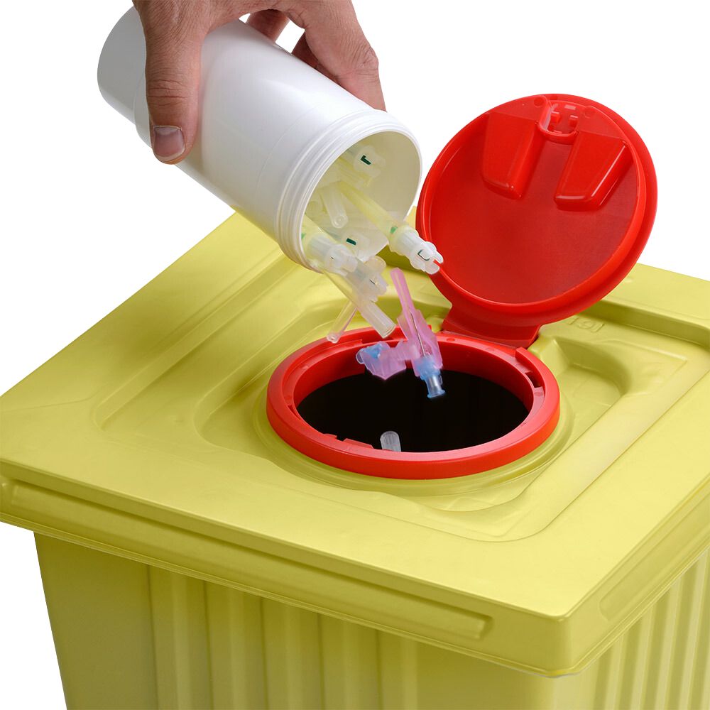 Een hand gooit gebruikte spuitnaalden weg uit een witte Helmut Schwarz GmbH melijekt afvalcontainer 12 L in een gele medische afvalcontainer met rood deksel, en zorgt zo voor een correcte verwijdering.