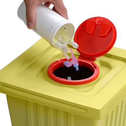 Een hand gooit gebruikte spuitnaalden weg uit een witte Helmut Schwarz GmbH melijekt afvalcontainer 12 L in een gele medische afvalcontainer met rood deksel, en zorgt zo voor een correcte verwijdering.